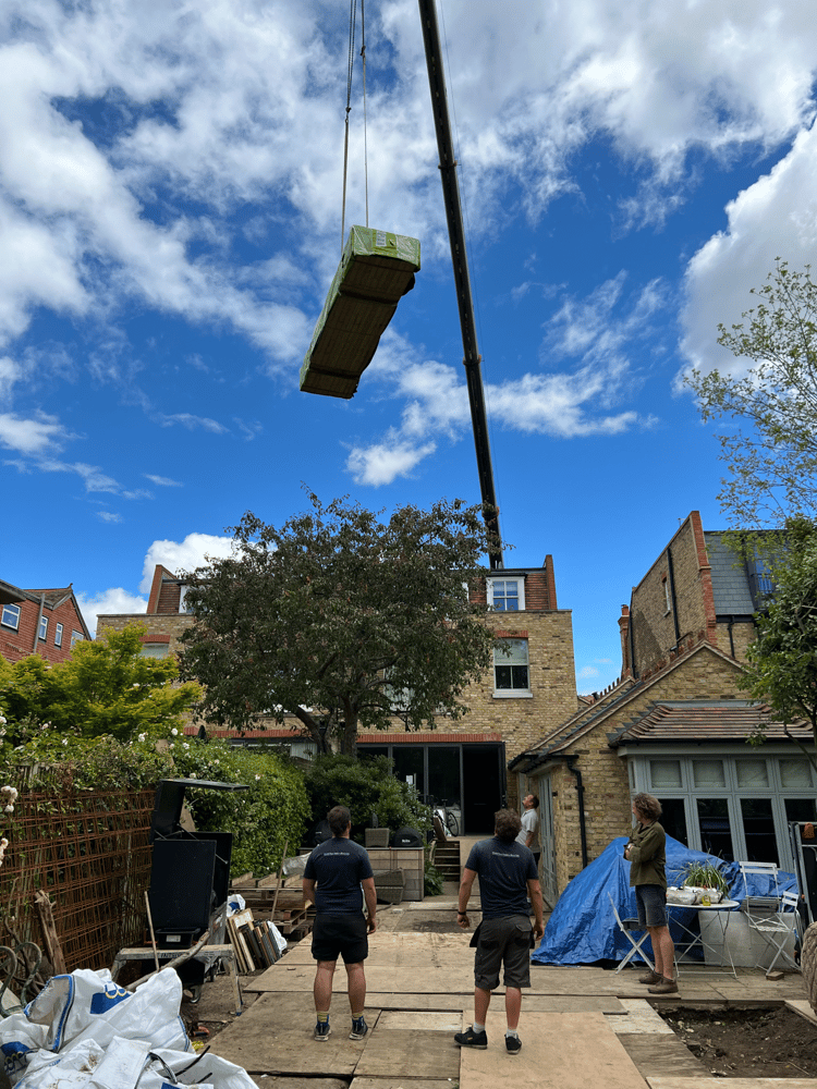 A crane lifts the materials for the garden room over the house