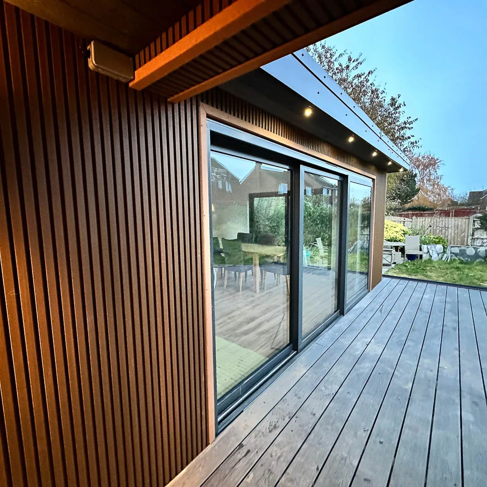 Teak coloured composite decking with a slatted profile contrasts with the aluminium Anthracite Grey doors and trims