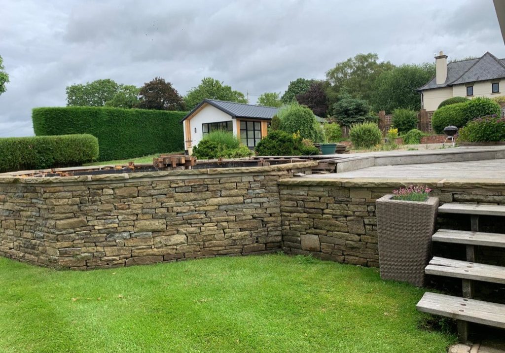 Swift Unlimited garden room with a white render gable, cedar and black glazing, above a new dry stone retaining wall